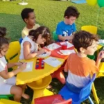 Kids are sitting at rounded table and playing with decoration colors at Splash N Bounce - Event Management Company in Dubai
